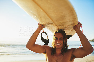 Buy stock photo Cropped portrait of a handsome young man smiling while carrying his surfboard over his head on the beach at sunset