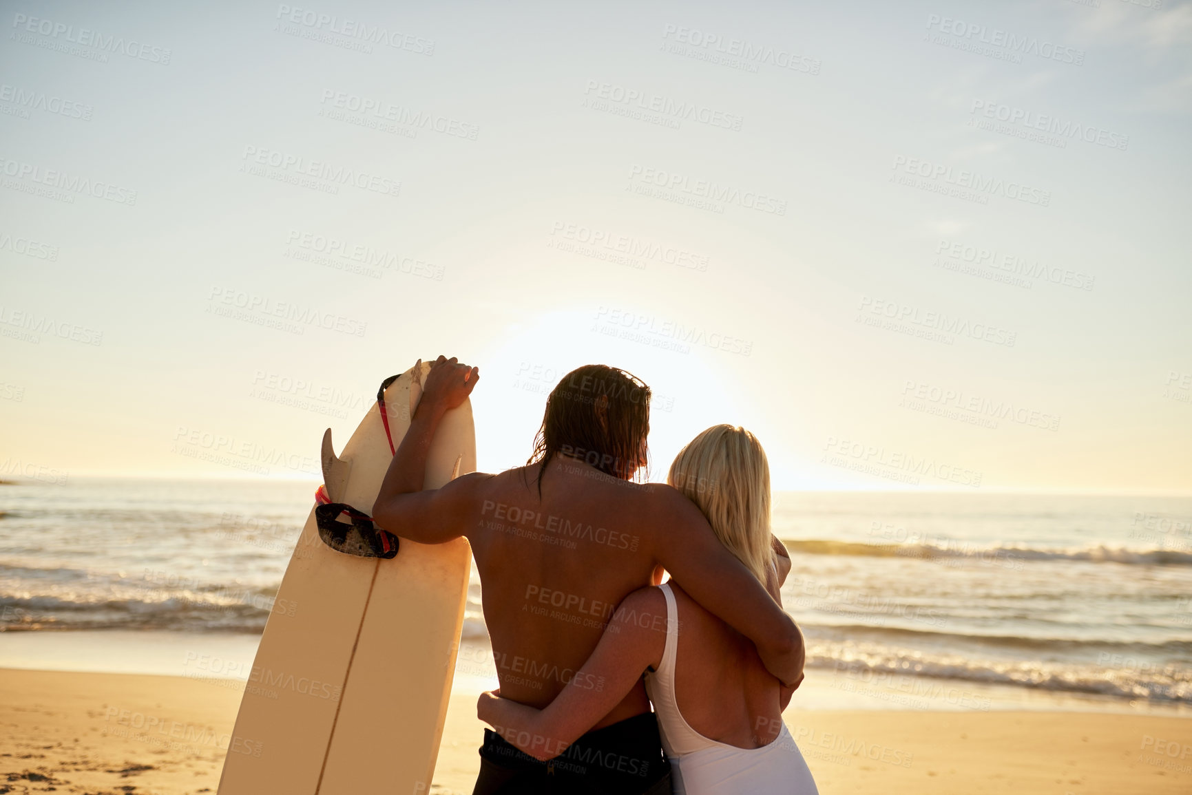Buy stock photo Cropped rearview shot of an unrecognizable young couple with a surfboard standing and holding each other on the beach