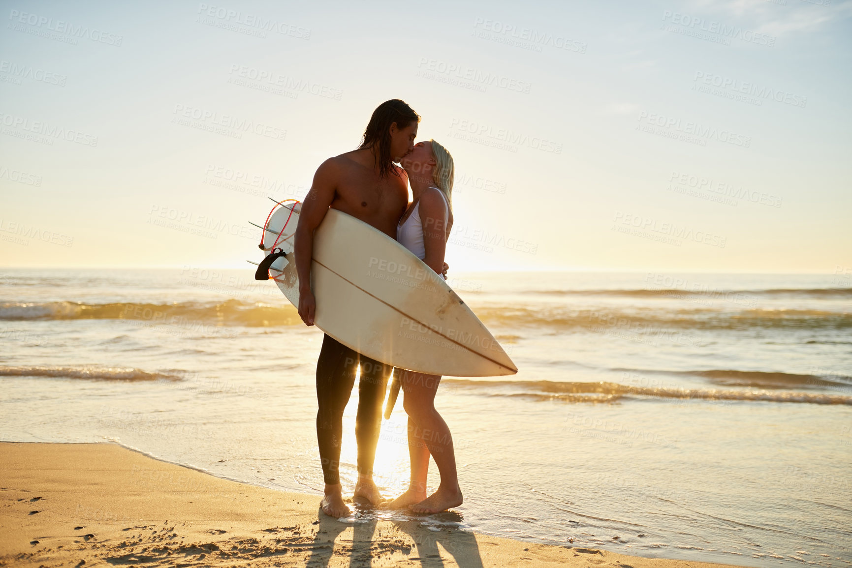 Buy stock photo Full length shot of an affectionate young couple with a surfboard kissing on the beach at sunset