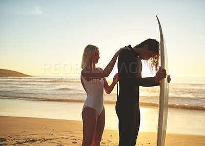 Buy stock photo Cropped shot of a young couple zipping up his wetsuit before going surfing at sunset