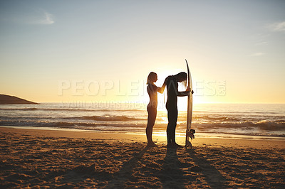 Buy stock photo Full length shot of a young couple zipping up his wetsuit before going surfing at sunset