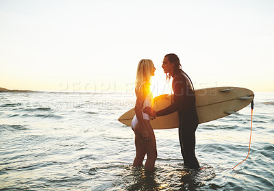 Buy stock photo Cropped shot of an affectionate young couple with a surfboard kissing on the beach at sunset
