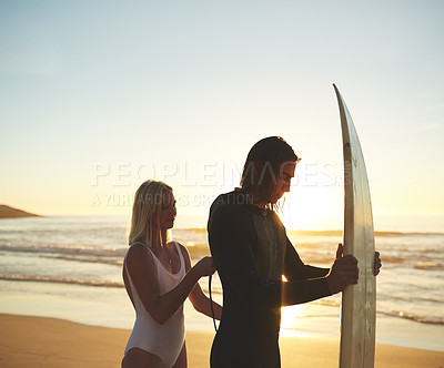 Buy stock photo Cropped shot of a young couple zipping up his wetsuit before going surfing at sunset