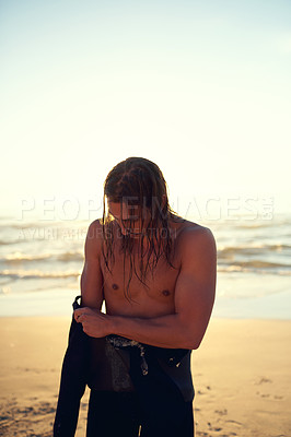 Buy stock photo Shot of a young man putting on a wetsuit at the beach