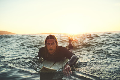 Buy stock photo Shot of a young man paddling on a surfboard in the sea