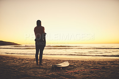 Buy stock photo Rearview of a young surfer putting on a wetsuit at the beach