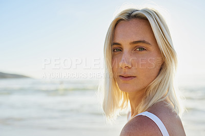 Buy stock photo Cropped portrait of an attractive young woman looking over her shoulder on the beach with the ocean behind her