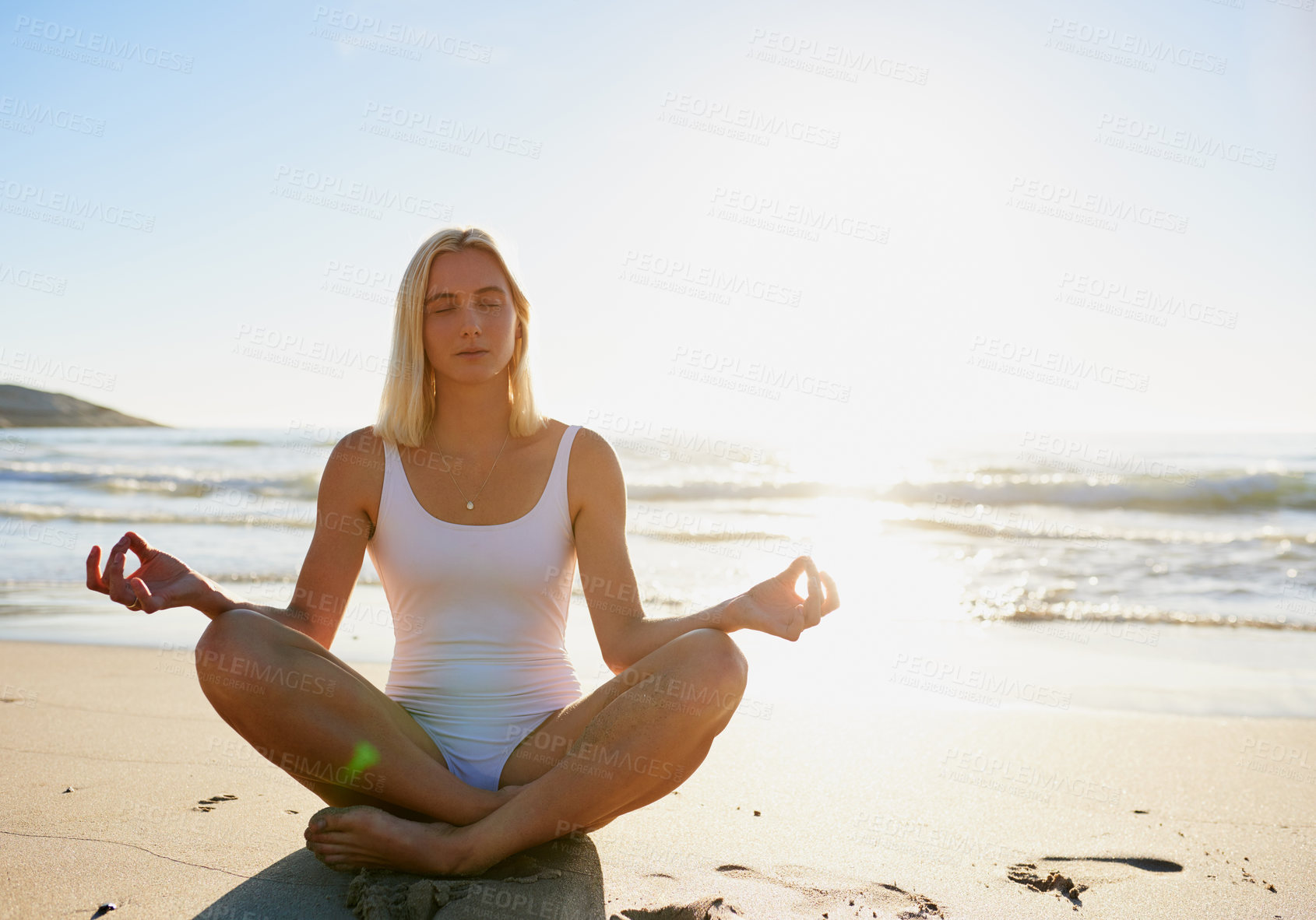 Buy stock photo Full length shot of an attractive young woman sitting with her legs crossed and meditating on the beach