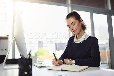 Buy stock photo Shot of an attractive young businesswoman sitting at her desk and writing notes in a modern office