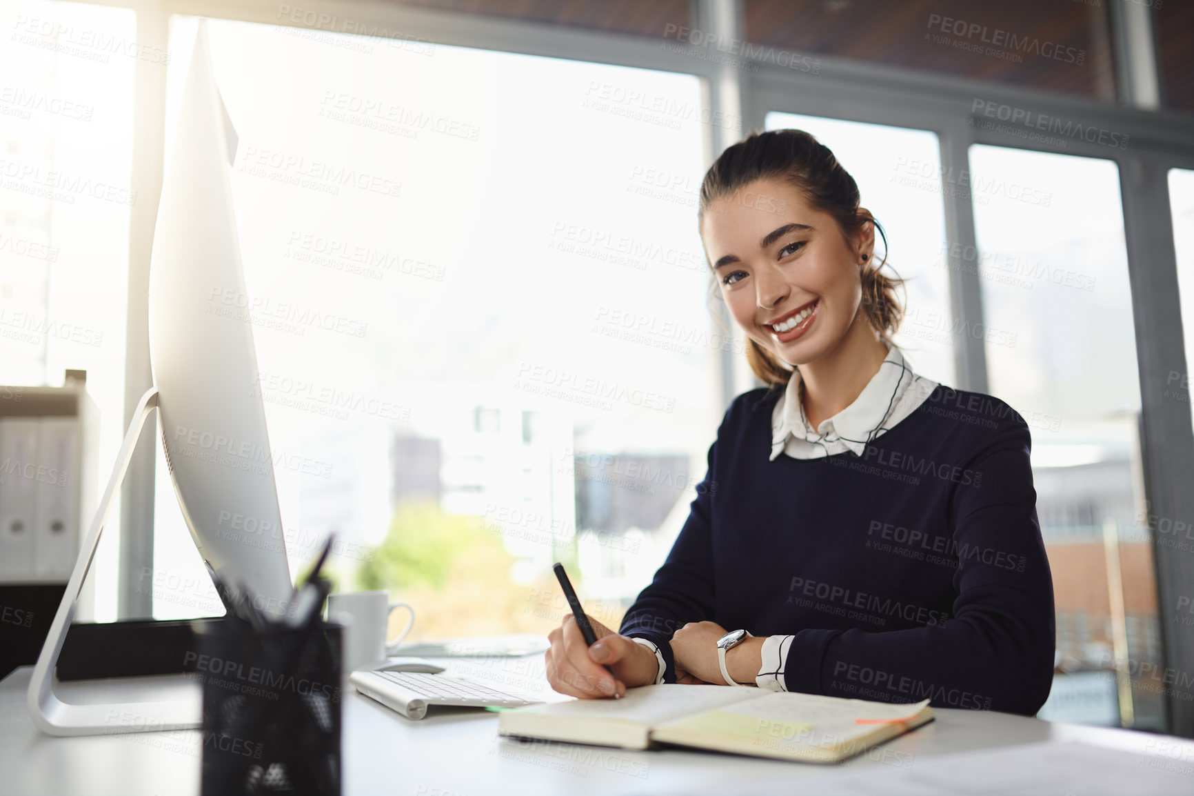 Buy stock photo Portrait of an attractive young businesswoman smiling and sitting at her desk while writing notes in a modern office
