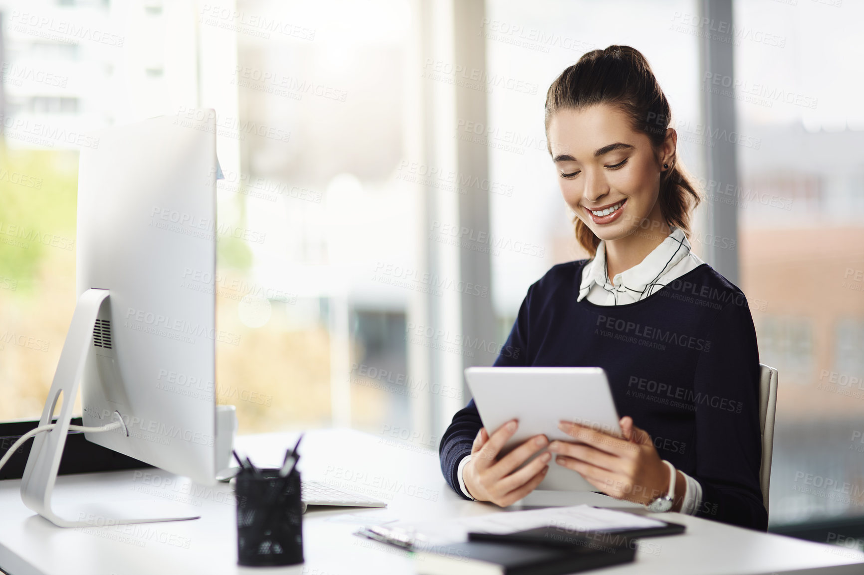 Buy stock photo Shot of an attractive young businesswoman sitting at her desk and using a tablet in a modern office