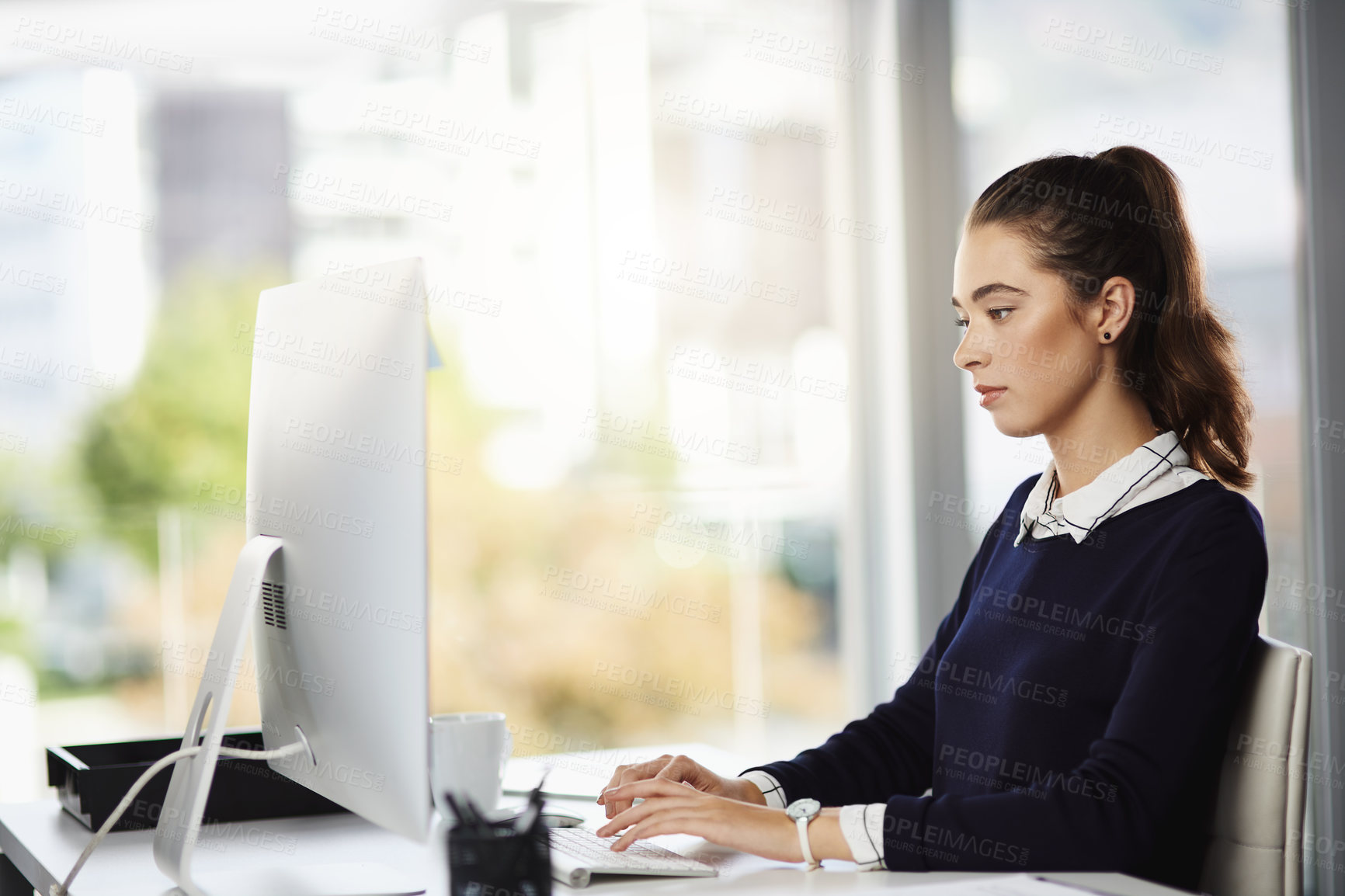 Buy stock photo Shot of an attractive young businesswoman sitting at her desk and using her computer in a modern office