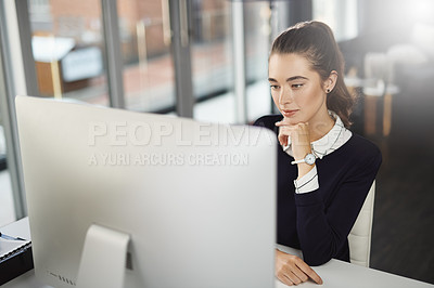 Buy stock photo Shot of an attractive young businesswoman sitting at her desk and looking at her computer screen in a modern office