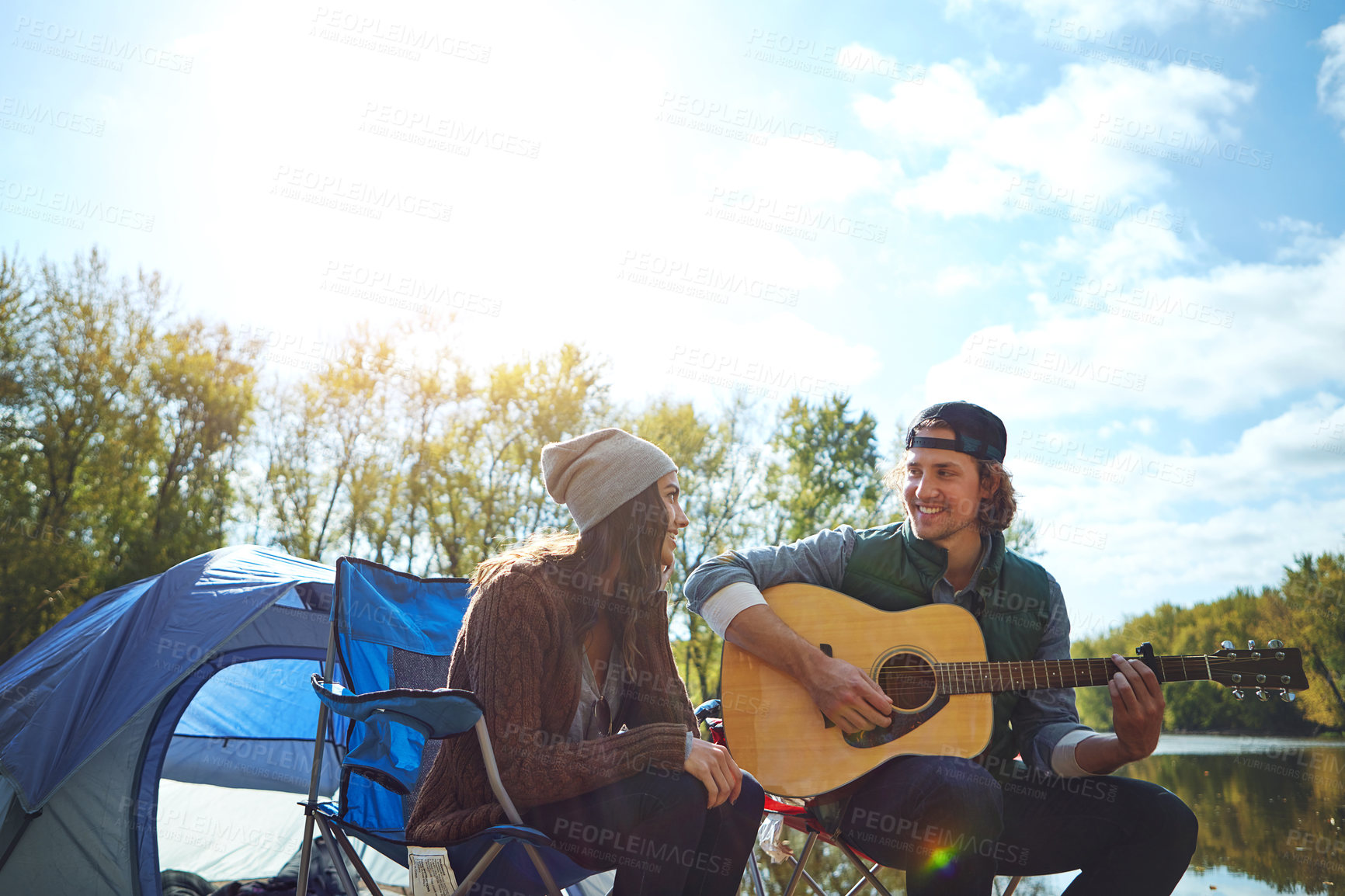 Buy stock photo Shot of a young man playing his girlfriend a song on his guitar while out camping