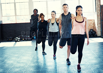 Buy stock photo Shot of a focused group of young people standing in a row and stretching before a workout session in a gym