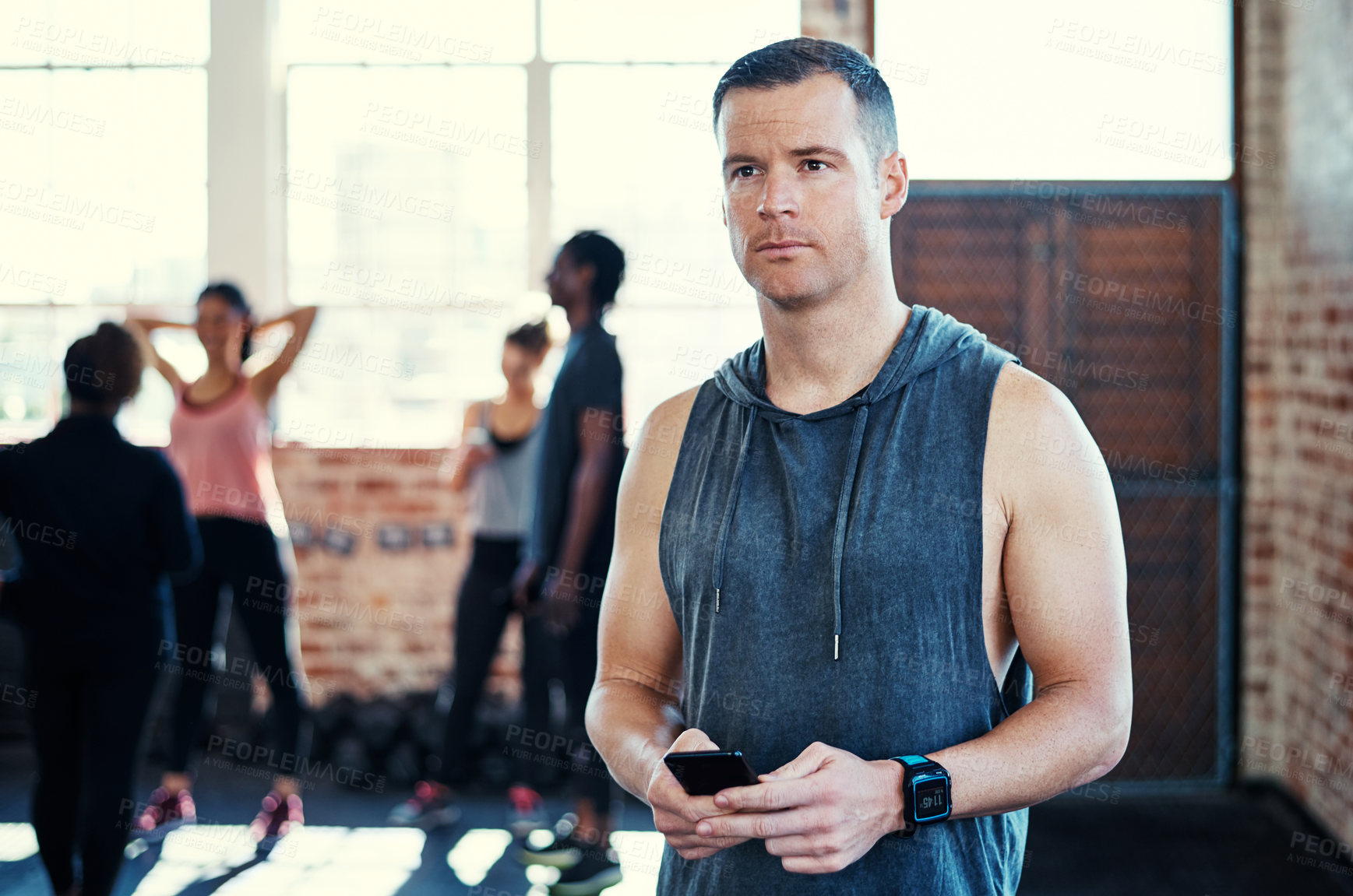 Buy stock photo Shot of a focused young man standing and using his cellphone while contemplating before a workout in a gym