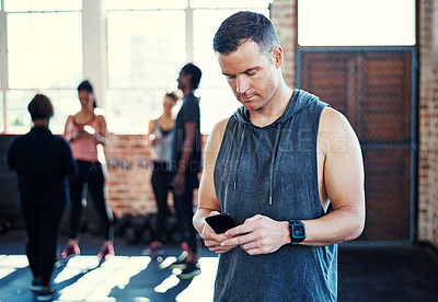 Buy stock photo Shot of a focused young man standing and using his cellphone before a workout in a gym