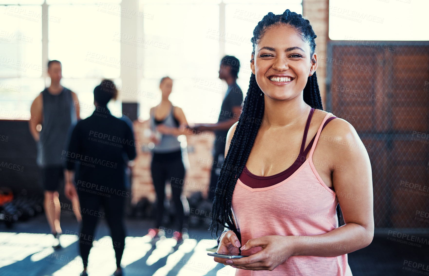 Buy stock photo Portrait of a cheerful young woman using her cellphone while looking into the camera before a workout in a gym
