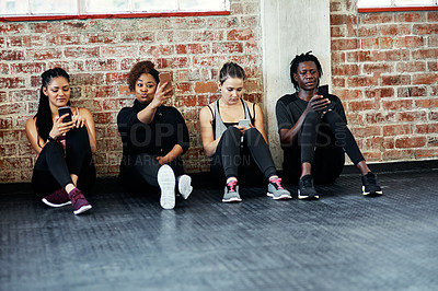 Buy stock photo Shot of a cheerful young group of people sitting down the floor and using their cellphones before a workout in a gym