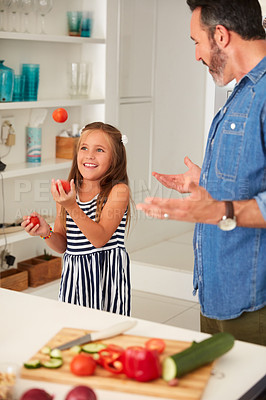 Buy stock photo Shot of an adorable little girl juggling tomatoes while cooking with her father at home
