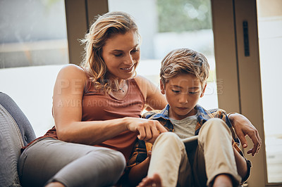 Buy stock photo Shot of an adorable little boy using a digital tablet with his mother on the sofa at home