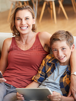 Buy stock photo Shot of an adorable little boy using a digital tablet with his mother on the sofa at home