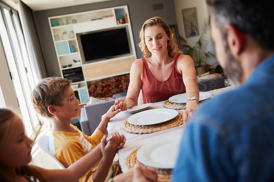 Buy stock photo Shot of a young family holding hands in prayer before having a meal together at home