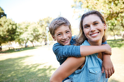 Buy stock photo Shot of an adorable little boy enjoying a piggyback ride with his mother in the park