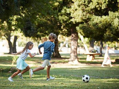 Buy stock photo Shot of an adorable little boy and girl playing soccer in the park