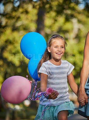 Buy stock photo Shot of an adorable little girl holding balloons and walking in the park with her mother