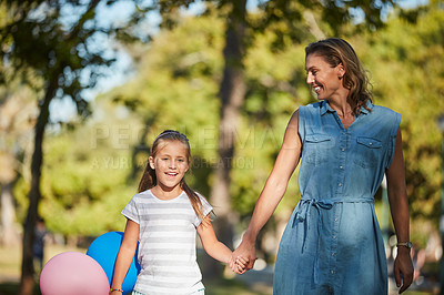 Buy stock photo Shot of an adorable little girl holding balloons and walking in the park with her mother