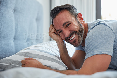 Buy stock photo Cropped portrait of an attractive mature man looking happy while lying on a bed at home in the morning