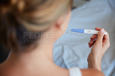 Buy stock photo High angle shot of an unrecognizable young woman holding a pregnancy test in her bedroom at home