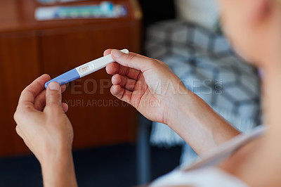 Buy stock photo High angle shot of an unrecognizable young woman holding a pregnancy test in her bedroom at home