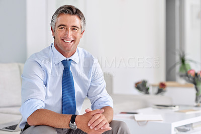 Buy stock photo Portrait of a confident mature businessman smiling and sitting on a sofa indoors with his hands clasped