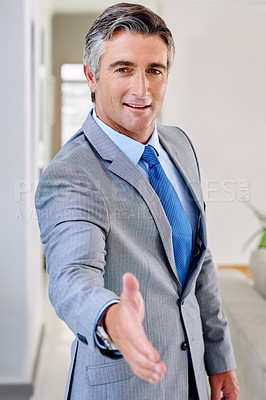 Buy stock photo Portrait of a mature businessman wearing a suit and standing indoors while extending his arm for a hand shake