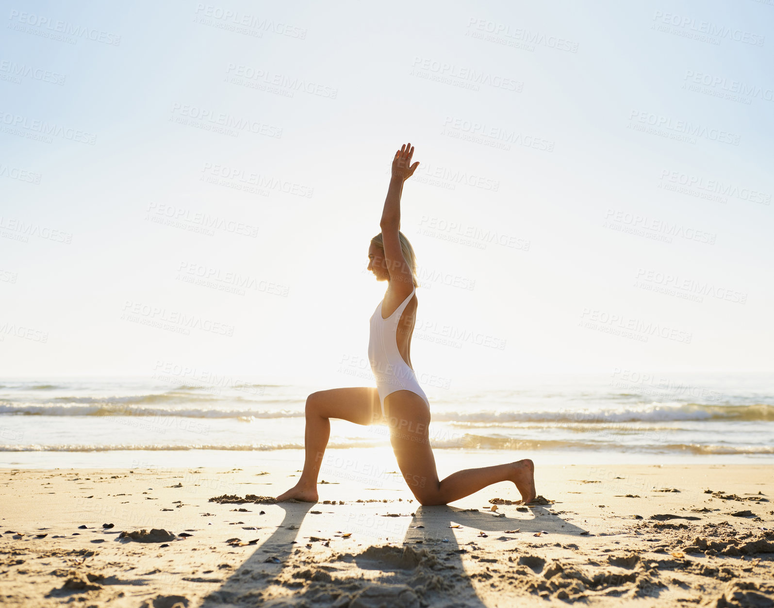 Buy stock photo Full length shot of an attractive young woman doing yoga early in the morning on the beach