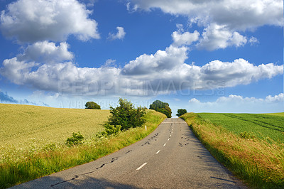 Buy stock photo Beautiful landscape of a countryside tar road with a cloudy blue sky and copy space. Roadway outdoors in nature on a summer afternoon or day near lush green grass with copyspace