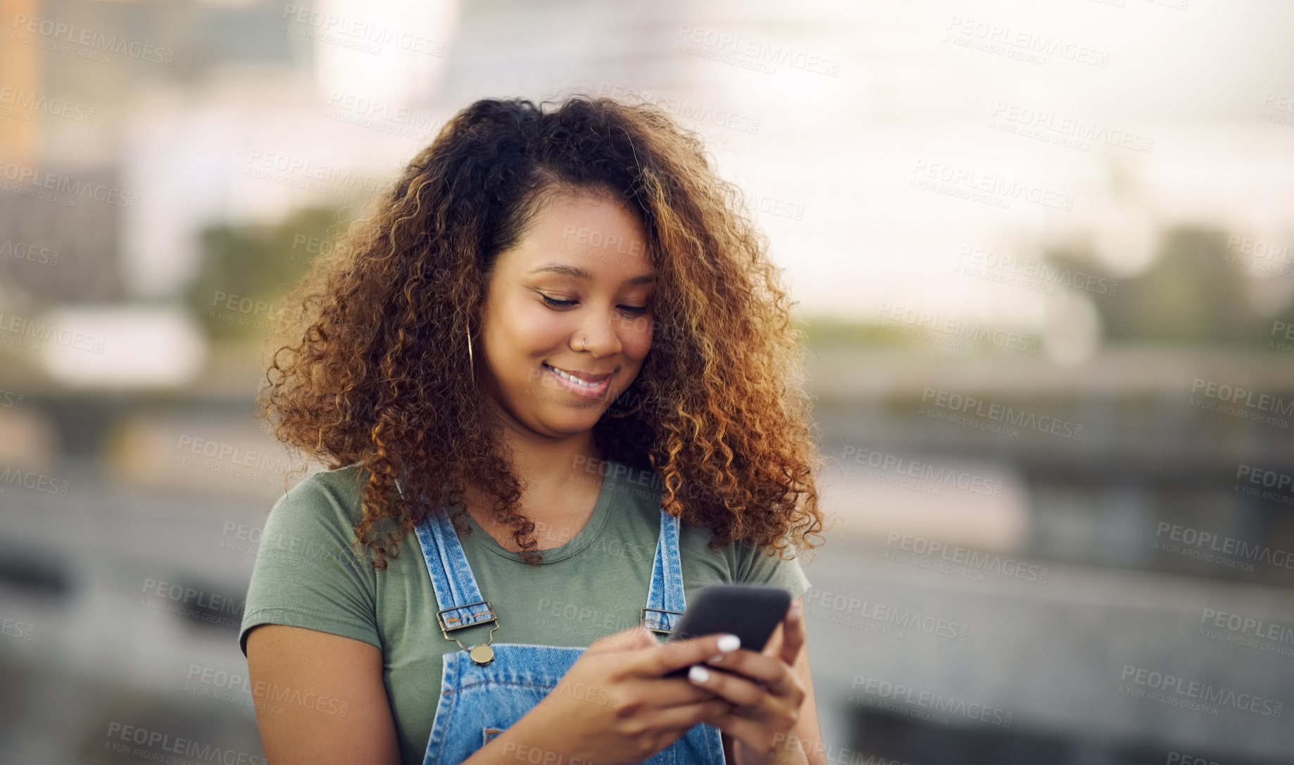 Buy stock photo Cropped shot of an attractive young woman standing outdoors and looking down while using her cellphone