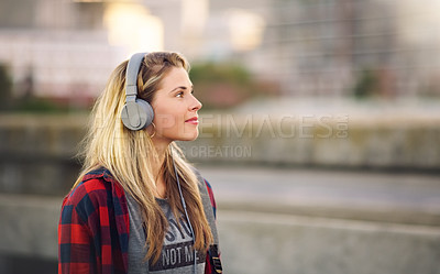 Buy stock photo Cropped shot of an attractive young woman walking down the street and listening to music through her headphones