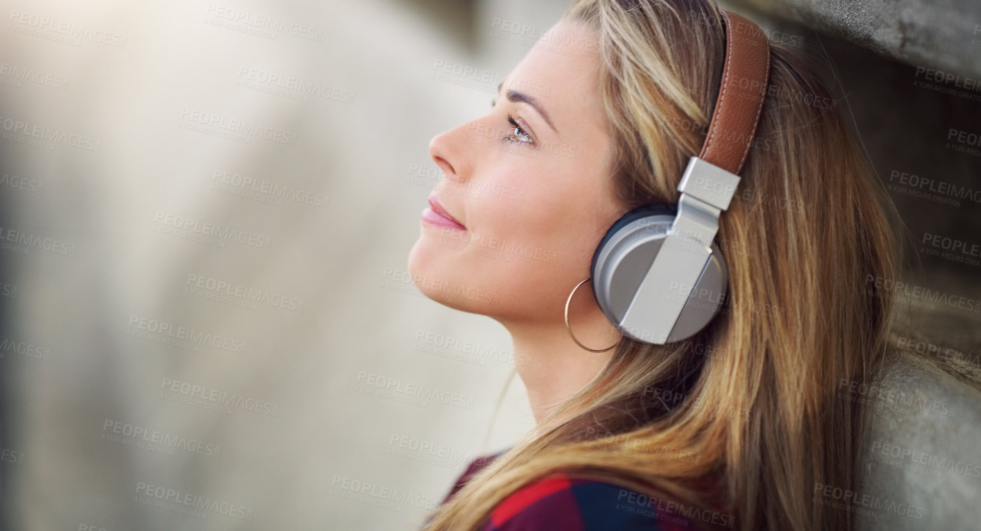 Buy stock photo Shot of an attractive young woman leaning against a wall and listening to music through her headphones