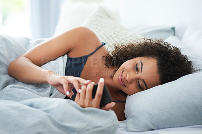 Buy stock photo Shot of an attractive young woman laying on her side in bed and using her mobile phone in the morning