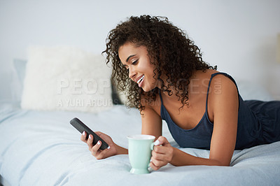 Buy stock photo Shot of an attractive young woman lying on her bed and using her cellphone while holding a coffee mug