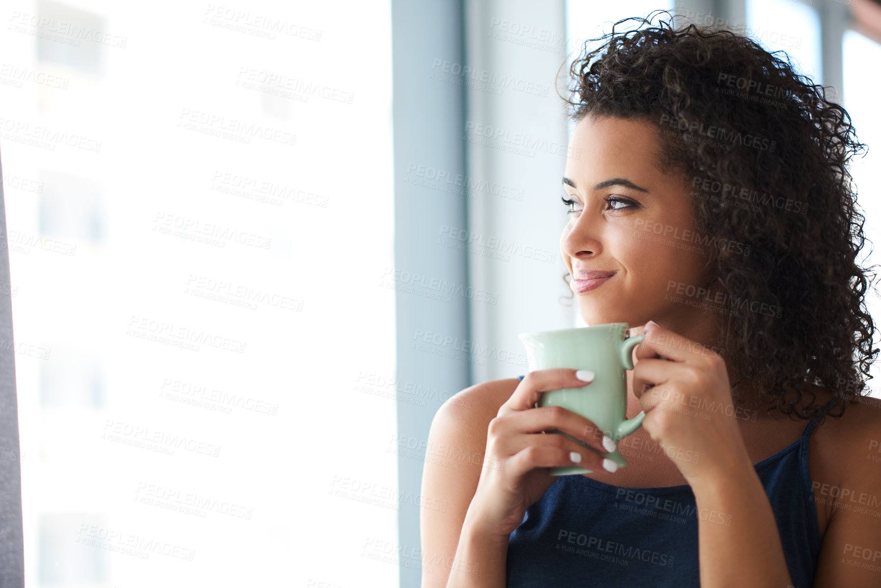Buy stock photo Shot of an attractive young woman holding a coffee mug and looking out the window in the morning