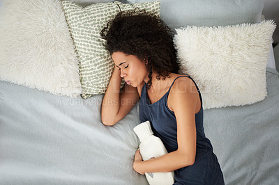 Buy stock photo Shot of an attractive young woman suffering from period cramps while lying in bed with a hot water bottle
