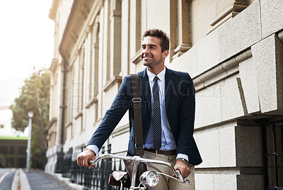 Buy stock photo Shot of a handsome young businessman pushing his bicycle while making his way to work in the morning