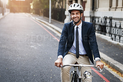 Buy stock photo Shot of a handsome young businessman riding his bicycle to work in the morning