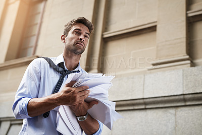 Buy stock photo Shot of a stressed out young man holding a heap of paper documents while walking to work in the morning