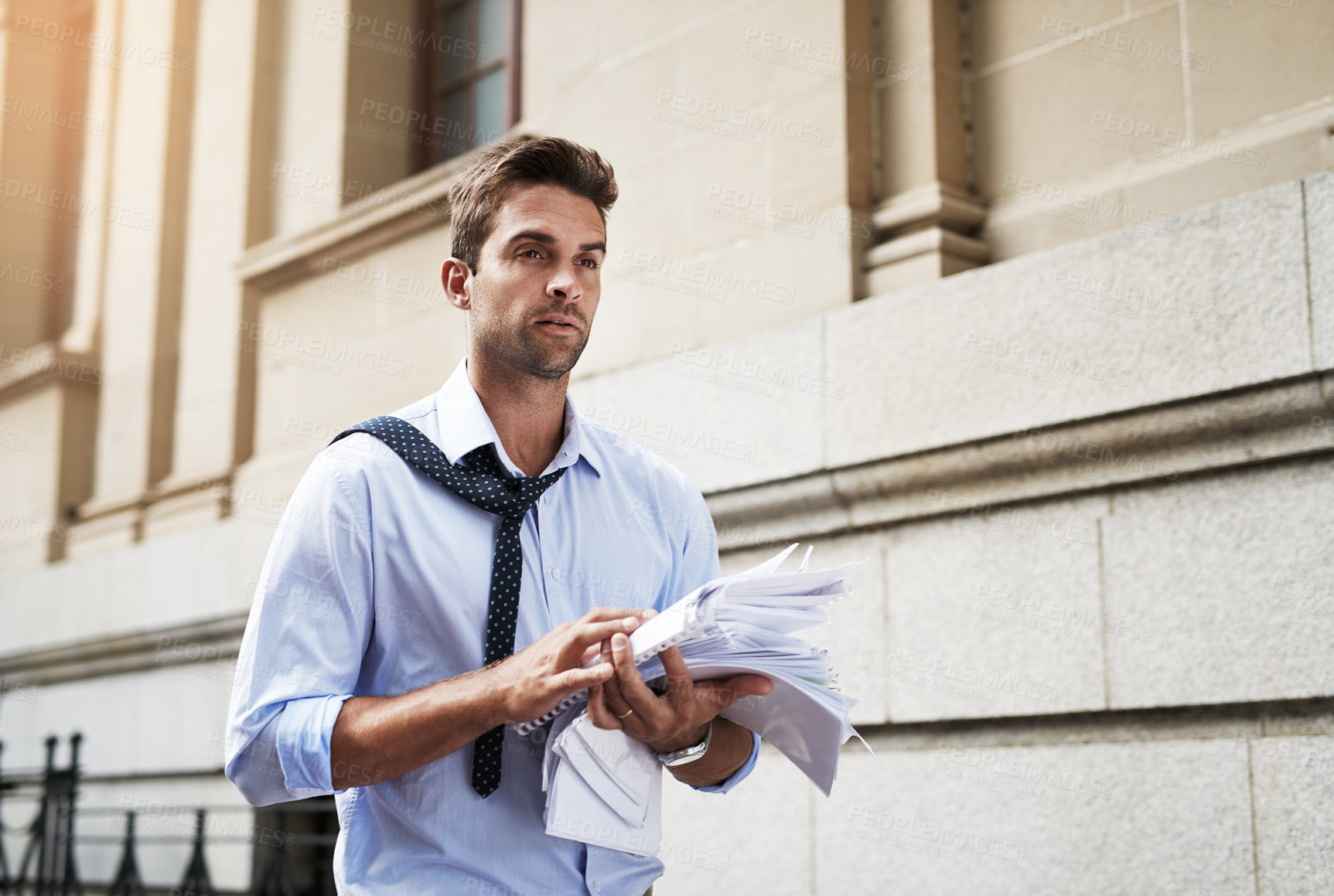Buy stock photo Shot of a stressed out young man holding a heap of paper documents while walking to work in the morning