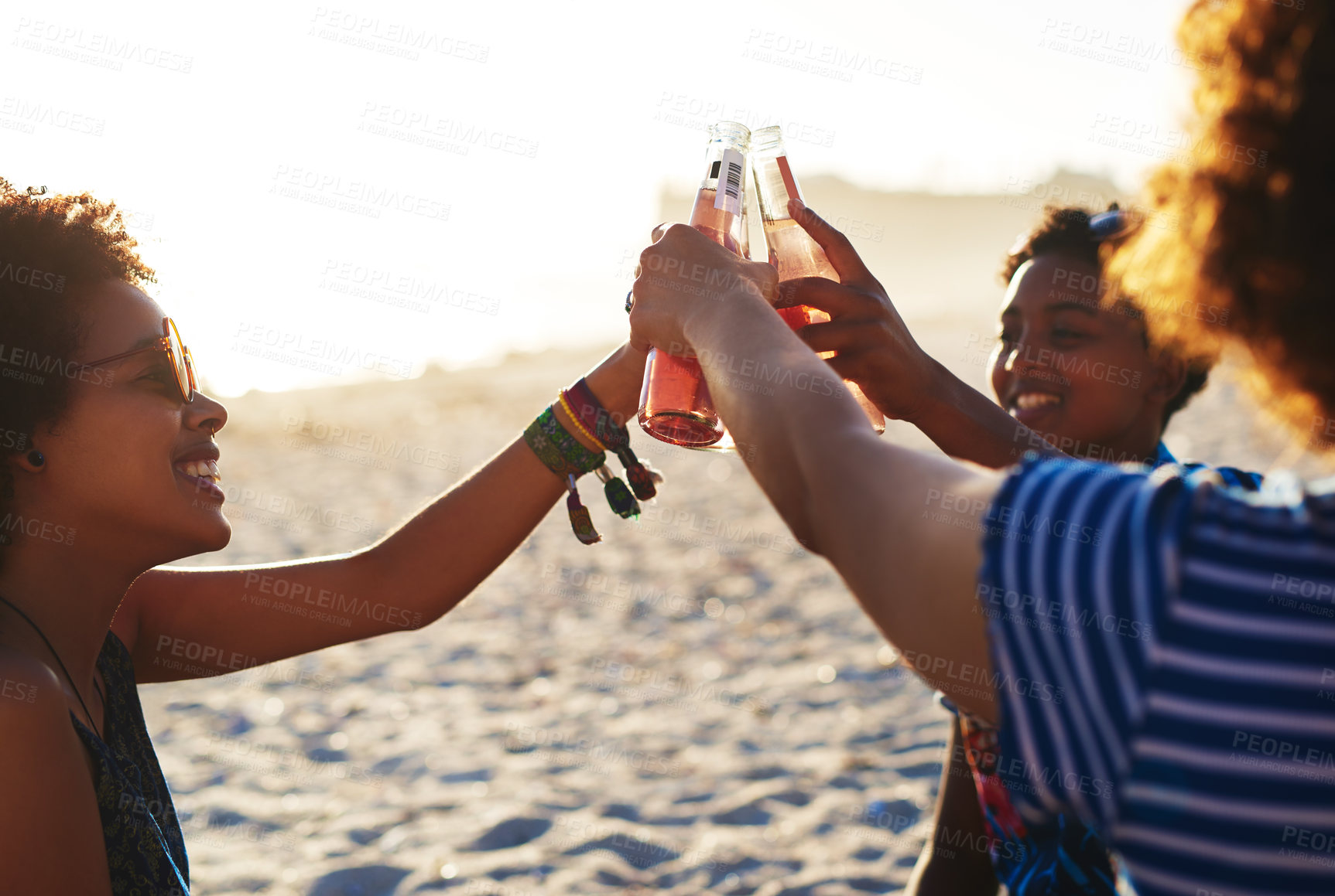 Buy stock photo Shot of an attractive young trio of women celebrating and having a drink together on the beach during the day